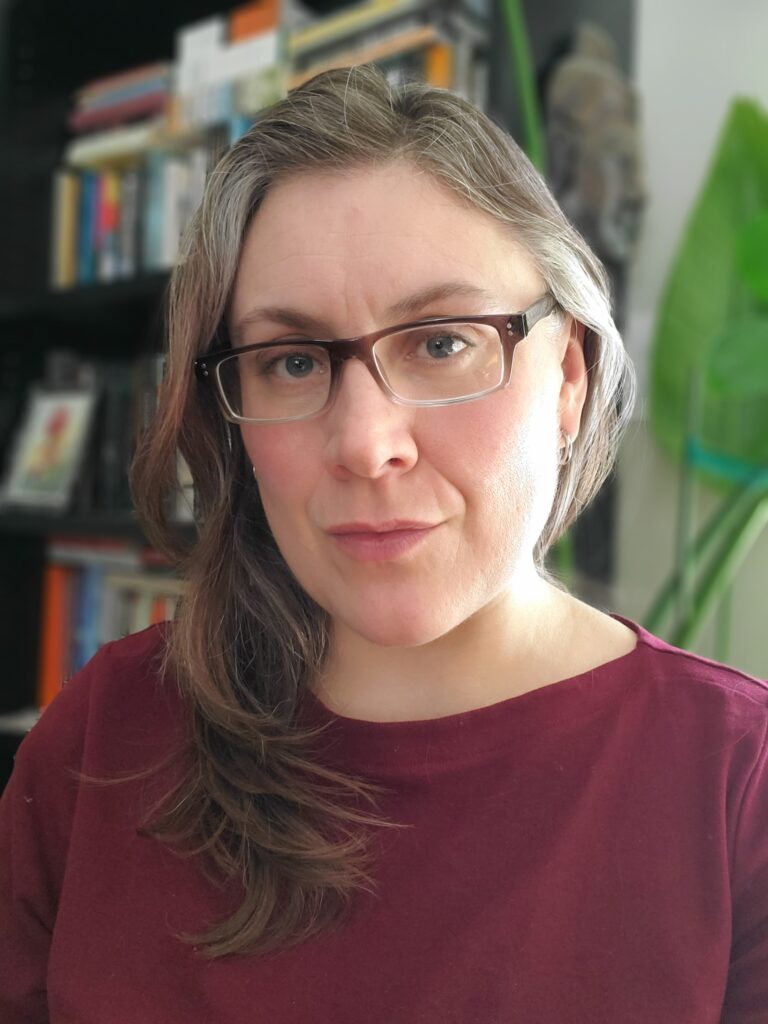 Photo of Arielle Smith, a woman with long gray hair and glasses, with a bookshelf in the background.