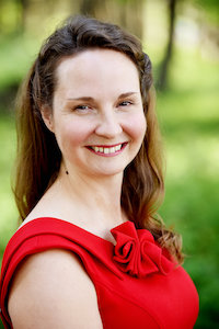 Photo of Chany Ockert wearing a bright red top with a blurred green background.