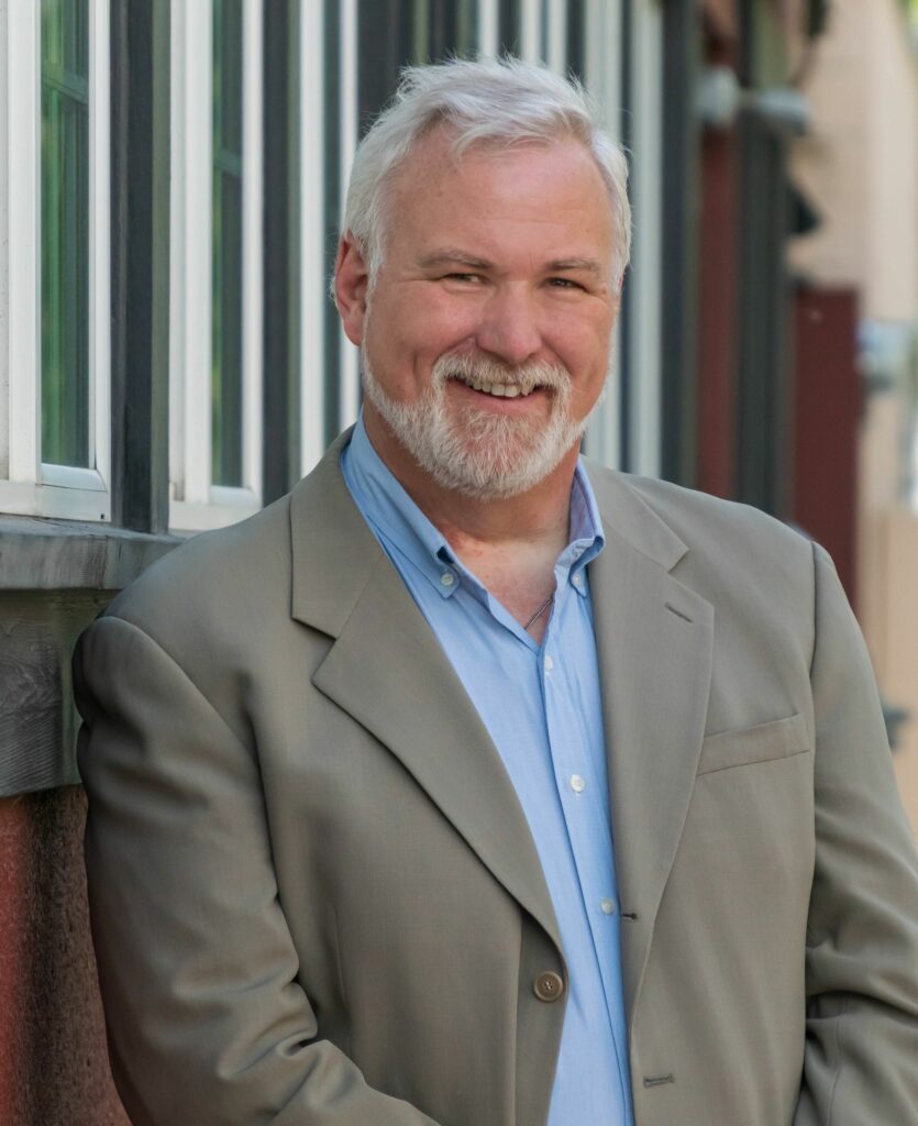 Headshot of Ned Cooney, a white man with gray beard, wearing a gray jacket and blue shirt.
